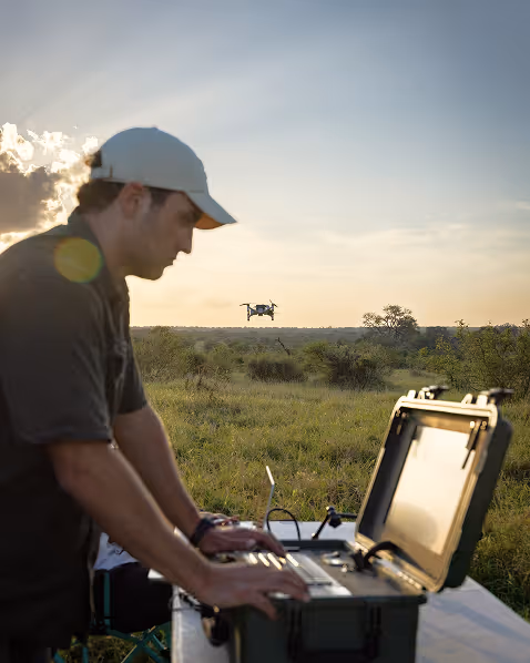 Man operating a drone outdoors using a laptop on a case in a grassy field at sunset.