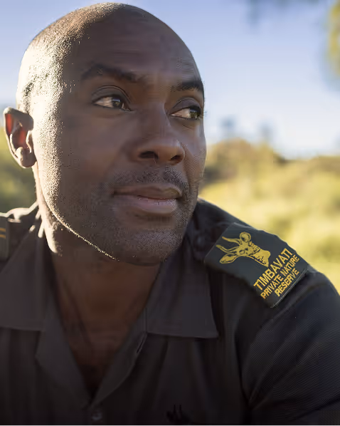 Man in a uniform for Timbavati Private Nature Reserve looking thoughtfully to the side outdoors.