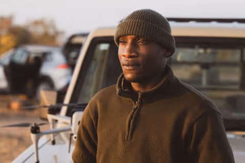 Man stands outdoors near vehicles in soft evening light.